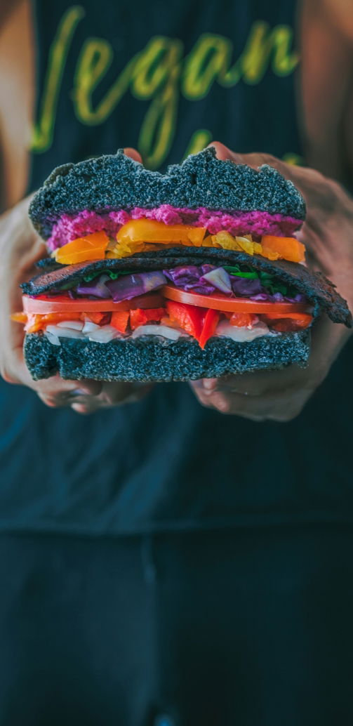 person holding meat sandwich with sliced tomatoes, onions, and grilled meat